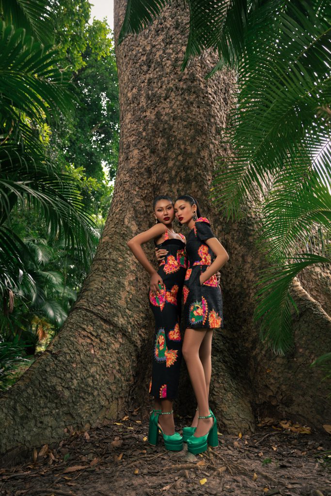 Hai người mẫu diện trang phục đen đỏ nổi bật tựa cây lớn trong vườn