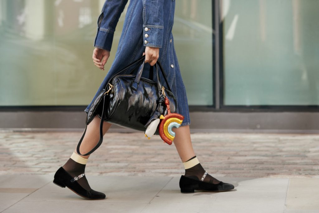 Cô gái đi giày đen vớ trắng đang cầm túi xách màu đen có dây đeo