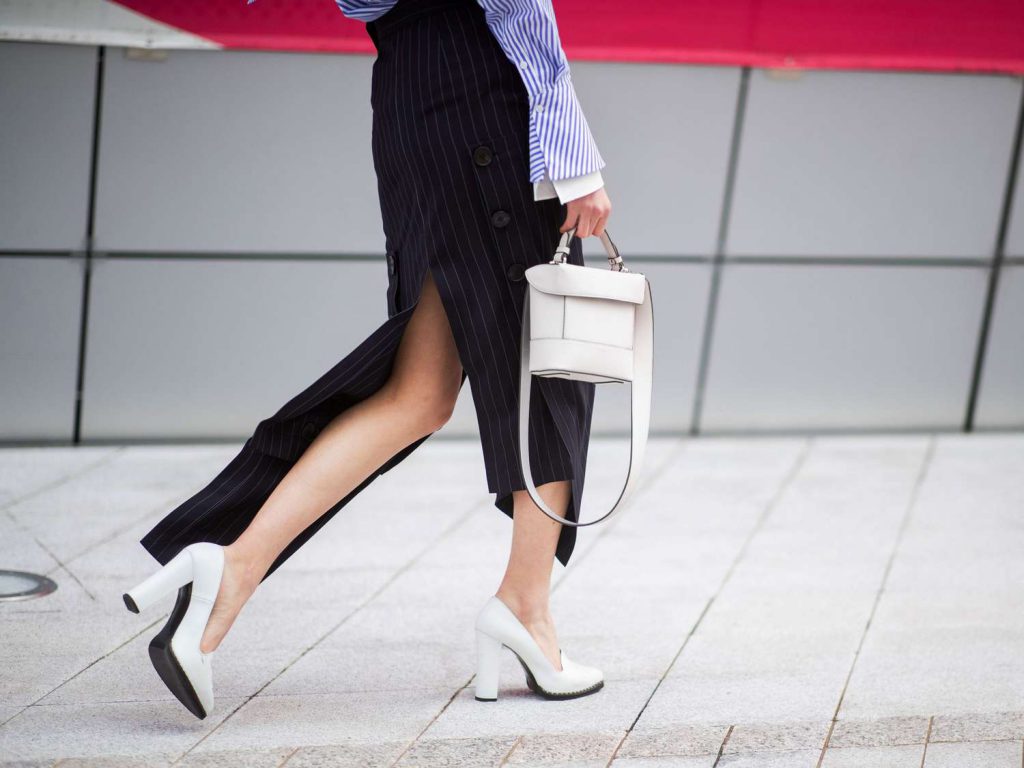 Người phụ nữ mặc váy xẻ tà và giày cao gót trắng đang đi trên phố