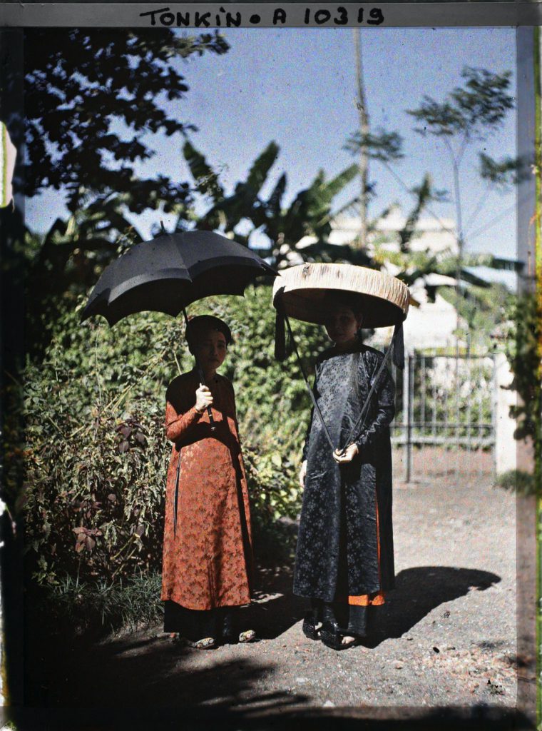 Hai phụ nữ mặc áo dài truyền thống che nắng bằng ô và nón lá