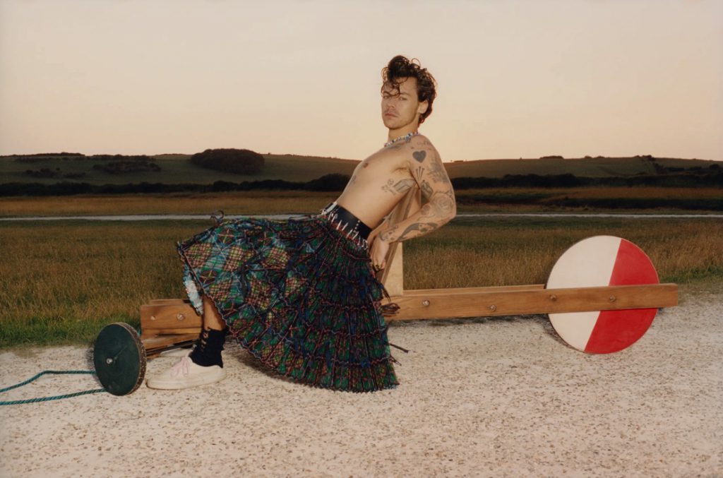 Người đàn ông ngồi trên một cỗ xe gỗ với váy karo và xăm hình