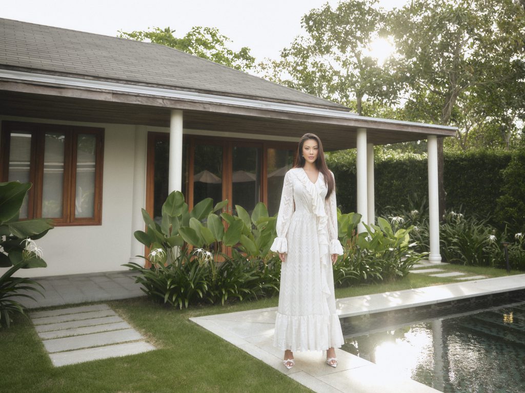 Người phụ nữ mặc váy trắng dài đứng trước một ngôi nhà hiện đại bên hồ bơi