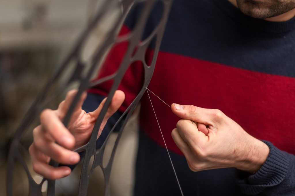 Người thợ tỉ mỉ khâu sợi chỉ lên khung vật liệu màu đen