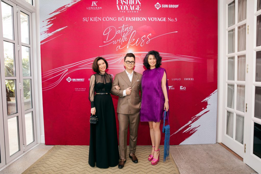 Ba người tạo dáng trước phông nền đỏ với dòng chữ "Dating with a kiss" tại sự kiện Fashion Voyage