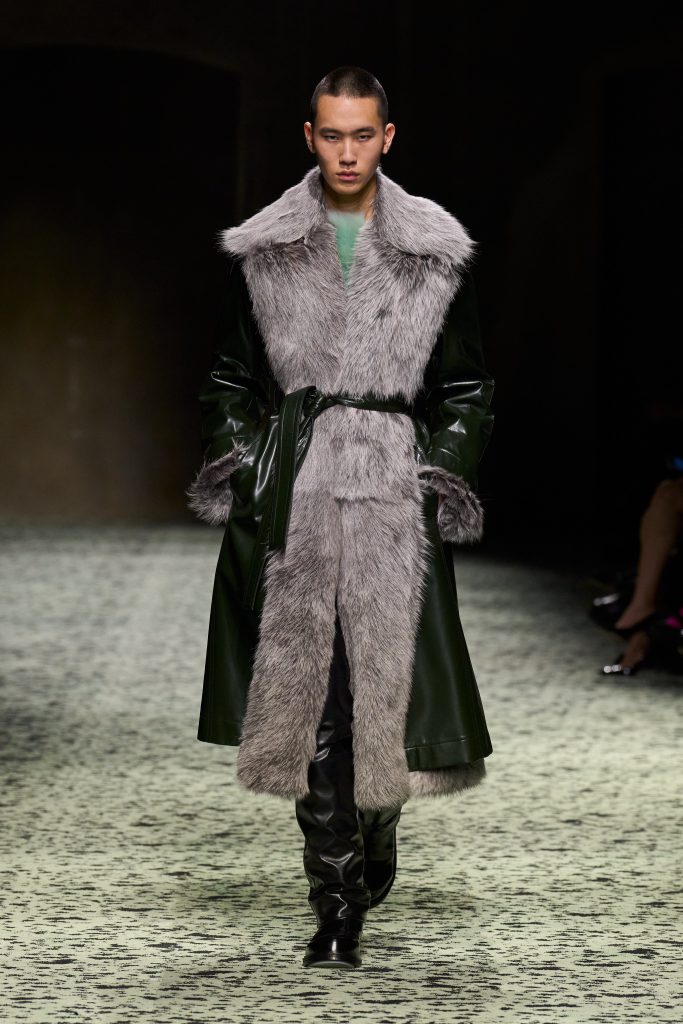 Người mẫu nam trình diễn áo khoác da xanh lá kết hợp lông xám trên sàn diễn thời trang