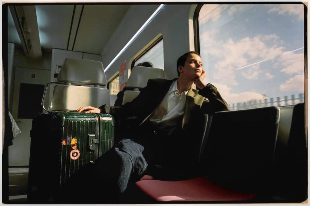 Người đàn ông ngồi trên tàu với hành lý RIMOWA và nhìn ra cửa sổ trời xanh