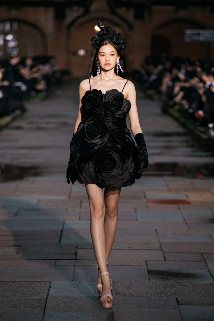 Người mẫu trình diễn váy đen đính hoa hồng và đội mũ tại show diễn thời trang