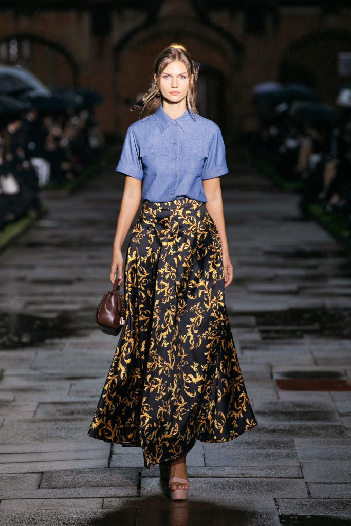 Người mẫu trình diễn trang phục áo sơ mi xanh và chân váy họa tiết vàng đen trên phố