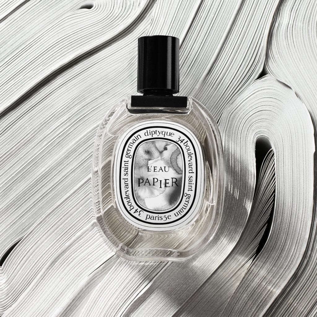 Chai nước hoa Diptyque L'Eau Papier nằm trên nền gỗ vân sáng