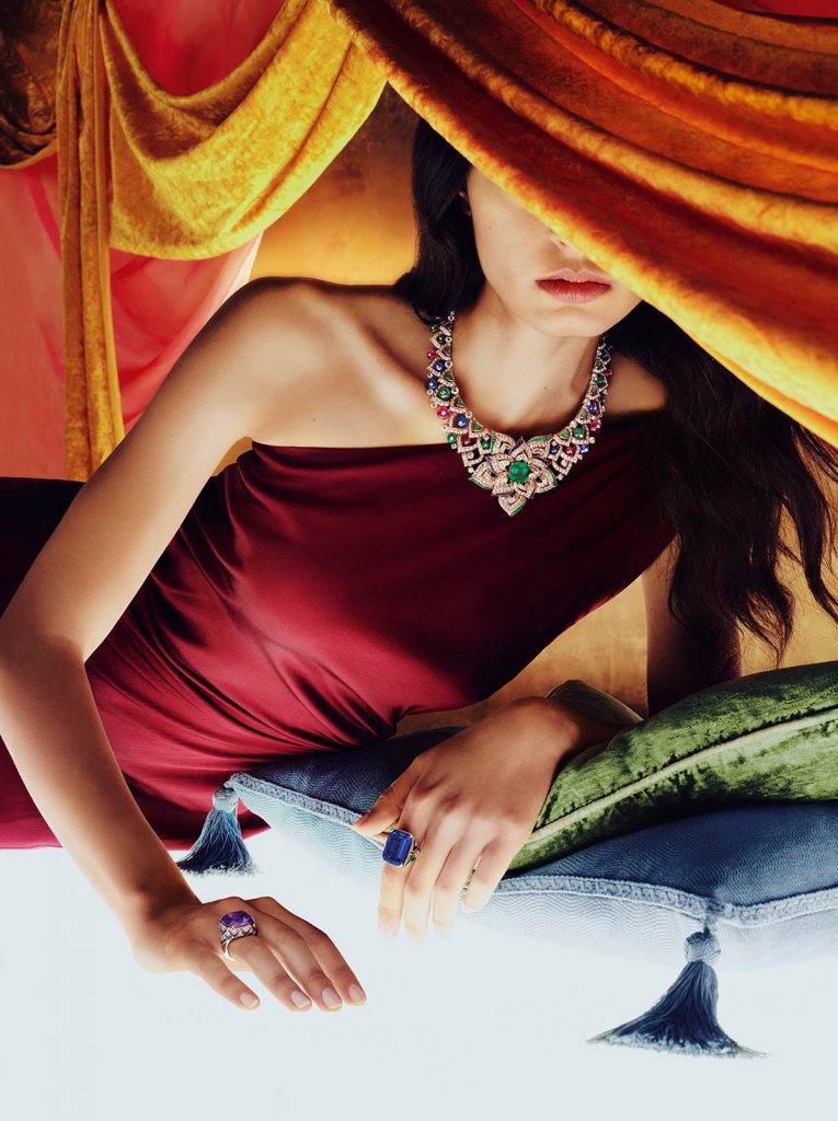 Người mẫu đeo trang sức lộng lẫy trên nền vải màu cam và gối xanh lam