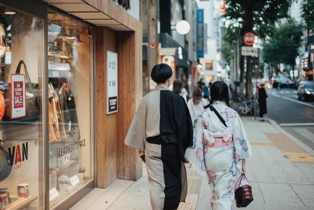 Hai người mặc kimono đi bộ trên phố với các cửa hàng hai bên đường