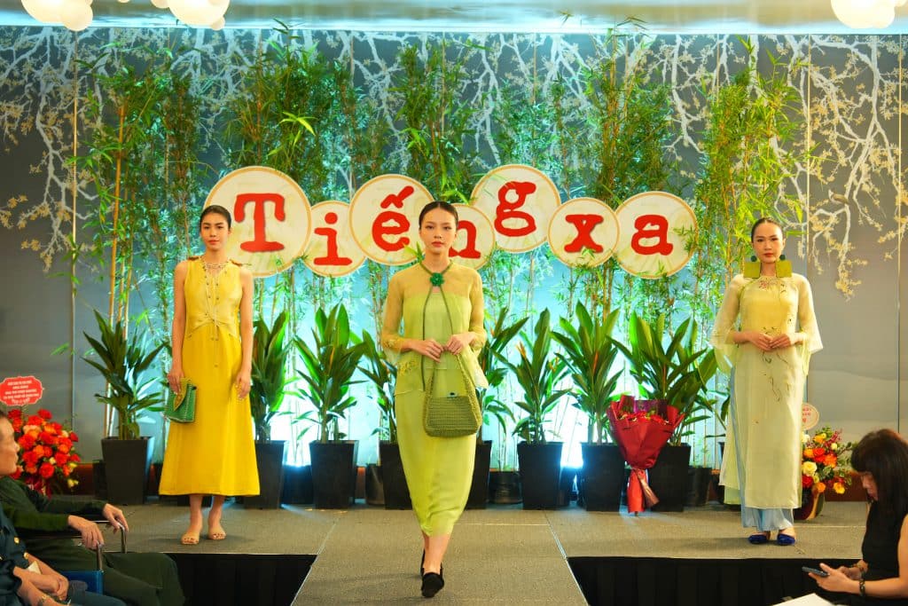 Ba người mẫu trình diễn áo dài vàng và xanh lục trên sàn diễn thời trang
