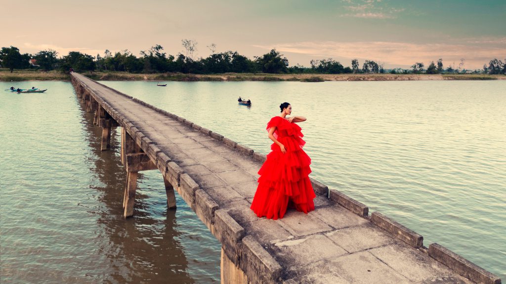 Người mẫu diện váy đỏ rực rỡ trên cầu bê tông trải dài qua mặt nước
