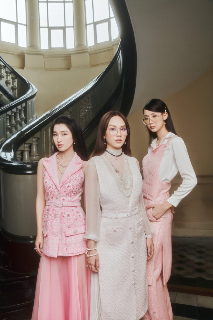 Ba phụ nữ mặc trang phục pastel đứng trước cầu thang xoắn ốc sang trọng