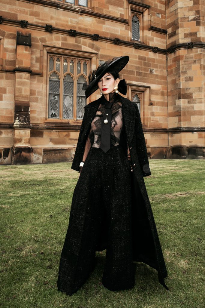 Người phụ nữ trung niên mặc trang phục đen thanh lịch trước một tòa nhà cổ kính