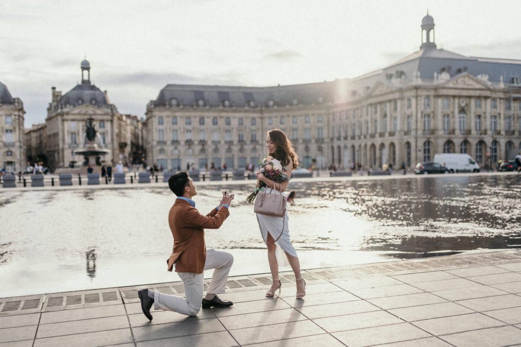 A man proposes to a smiling woman near the fountain at Place de la Bourse