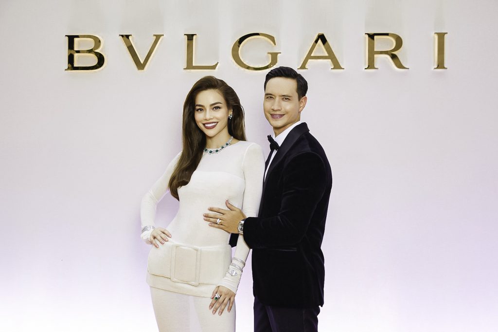 Hồ Ngọc Hà và một người đàn ông lịch lãm tạo dáng trước phông nền logo BVLGARI