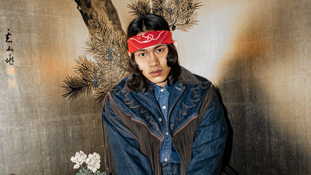 Người mẫu nam mặc áo denim và khăn đỏ trước nền tranh phong cảnh truyền thống