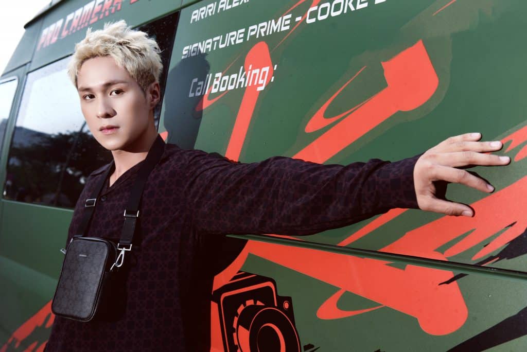 Nam người mẫu trẻ với áo khoác đen và túi xách tạo dáng trên nền xanh lá cây