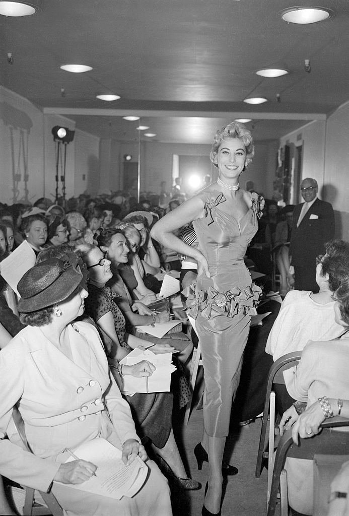 A model walks a runway past seated audience members during a vintage fashion show