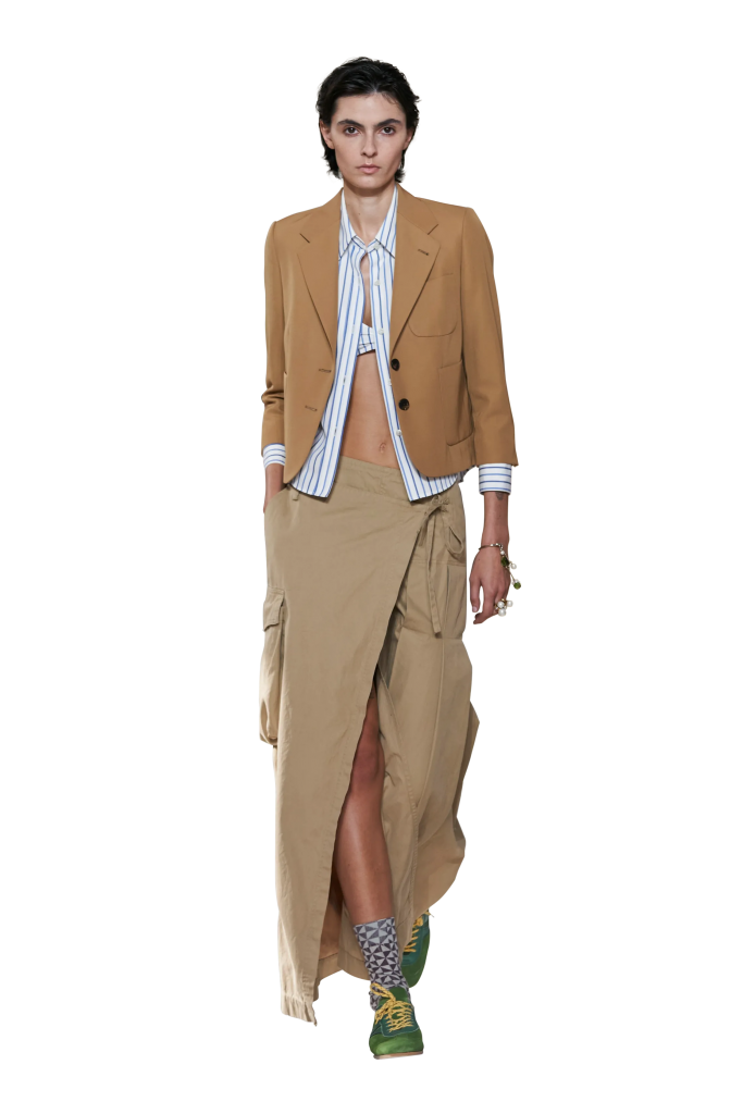 Người mẫu diện áo blazer nâu mở cùng áo sơ mi sọc xanh và chân váy dài xếp ly