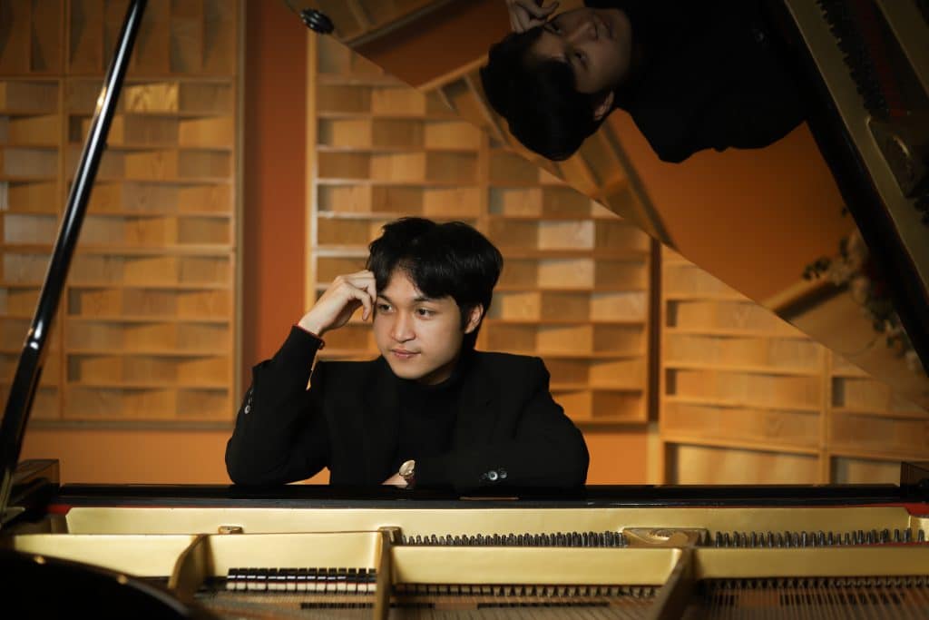 Người đàn ông trẻ ngồi trước cây đàn piano đen bóng với ánh đèn vàng ấm áp