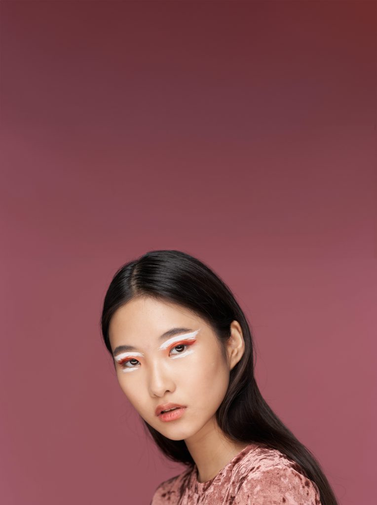 Cô gái châu Á với trang điểm mắt màu cam trắng nổi bật trên nền hồng phấn