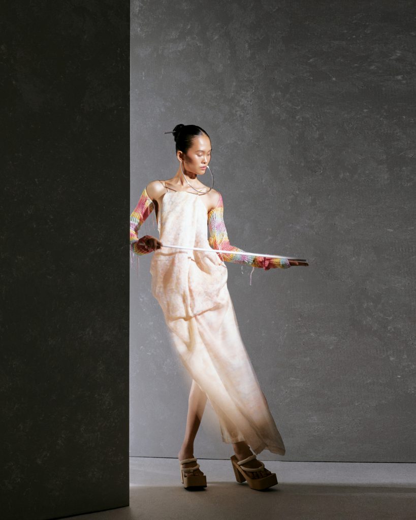 Người mẫu mặc váy dài tay áo màu nổi đang tạo dáng bên cột bê tông