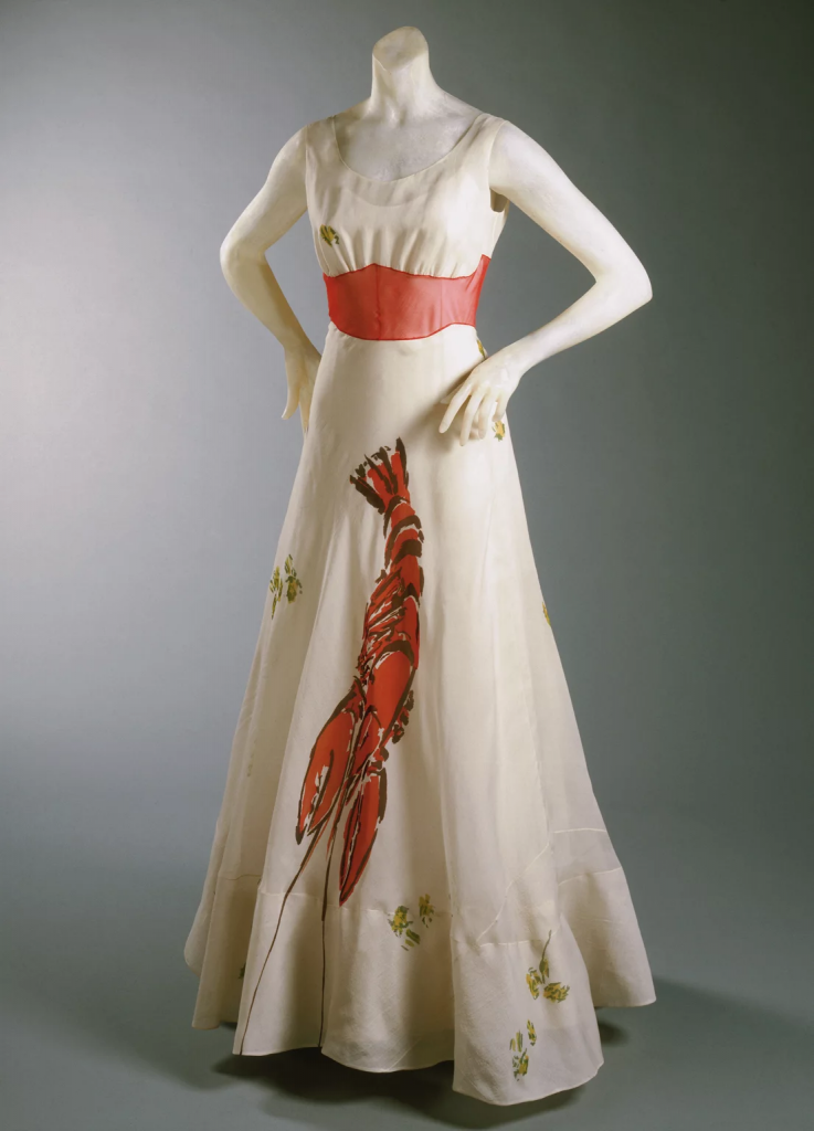 A white gown features a large lobster design and a red waistband on a mannequin