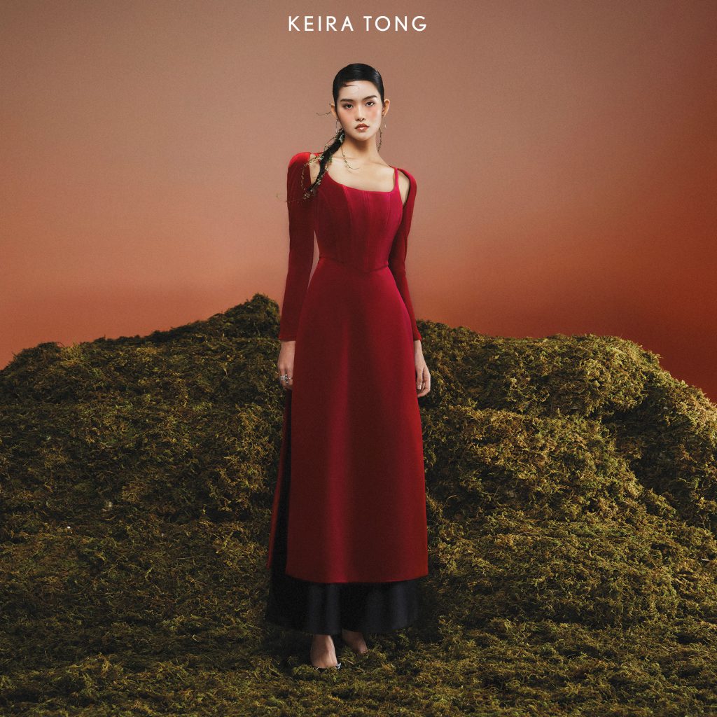 Người mẫu mặc áo dài đỏ đứng trên thảm cỏ xanh rêu