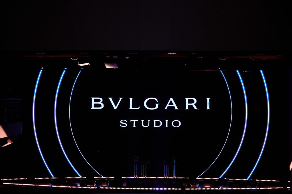 Logo BVLGARI STUDIO phát sáng trên nền đen với hai đường cong ánh sáng xanh hai bên