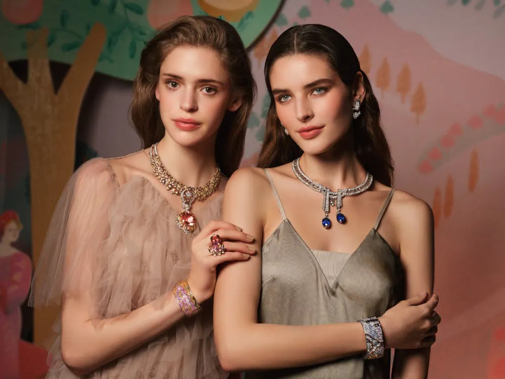 Hai người mẫu nữ trang điểm xinh đẹp đeo trang sức lấp lánh trước nền tranh sơn dầu