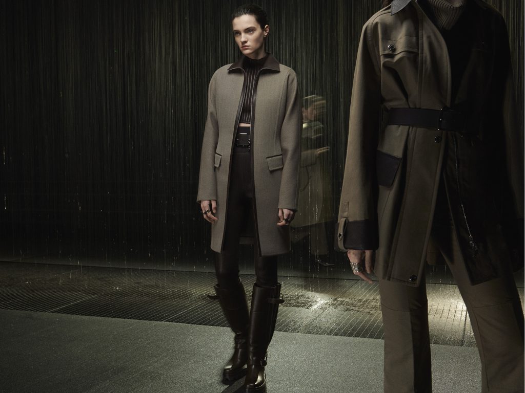 Người mẫu mặc áo khoác dài và quần bó đứng dưới mưa đêm đô thị