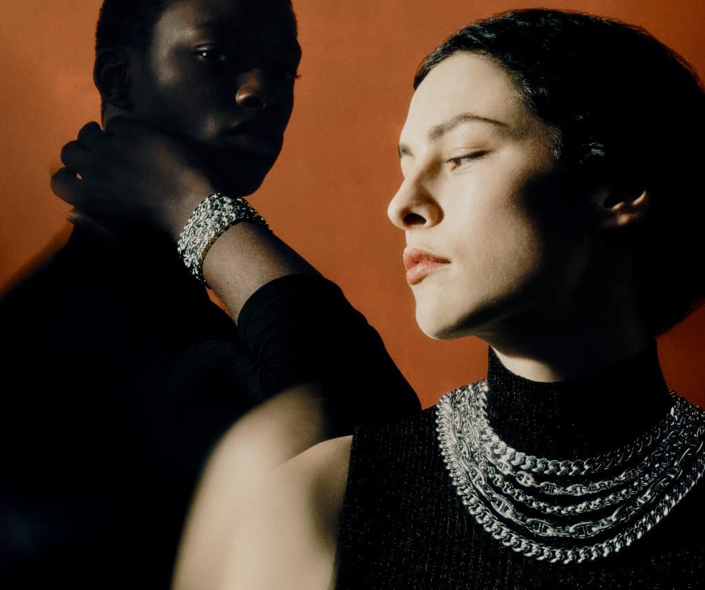 Hai người mẫu đeo trang sức Hermes Chaine d'ancre trên nền cam nổi bật