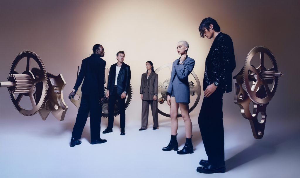 Nhóm người mặc trang phục lịch sự tạo dáng bên các bánh răng đồng hồ lớn