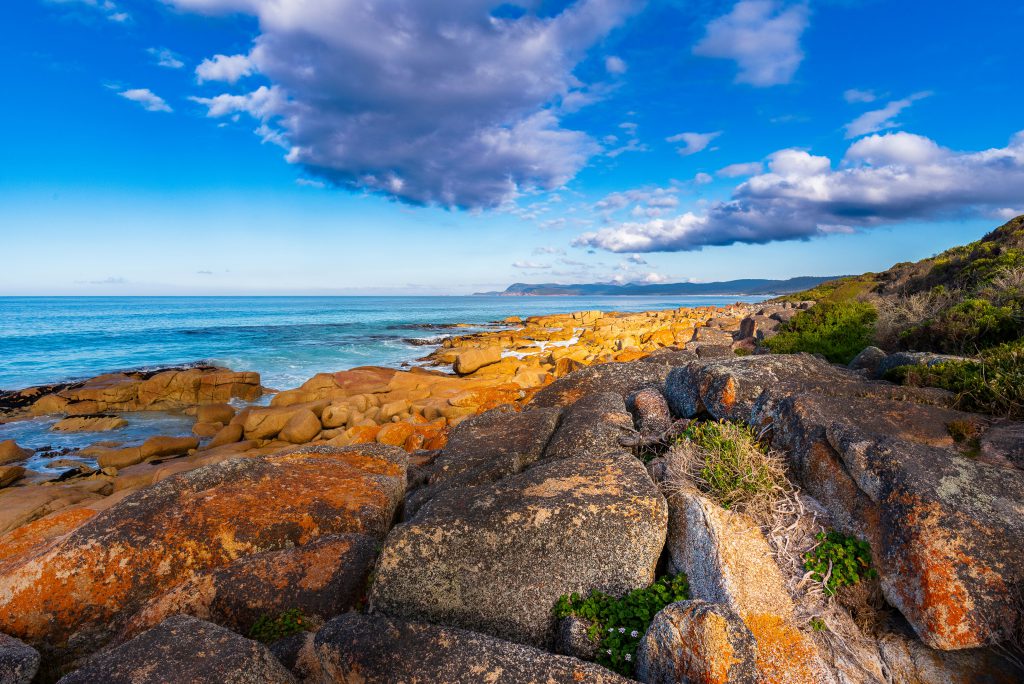 Rocky coastline meets turquoise water under a bright blue cloudy sky