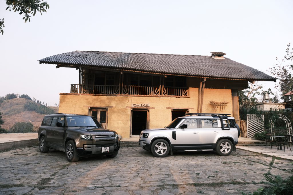 Hai xe Land Rover đỗ trước một ngôi nhà sàn truyền thống có kiến trúc độc đáo
