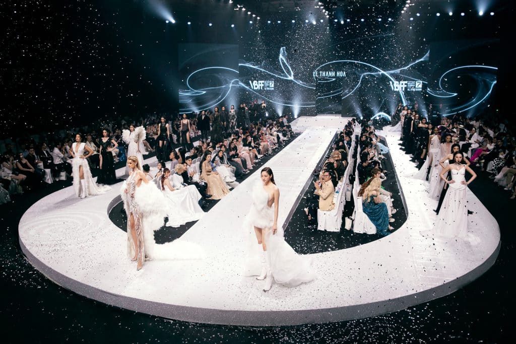 Sàn diễn thời trang với các người mẫu trình diễn trang phục trắng và nhiều màu sắc khác