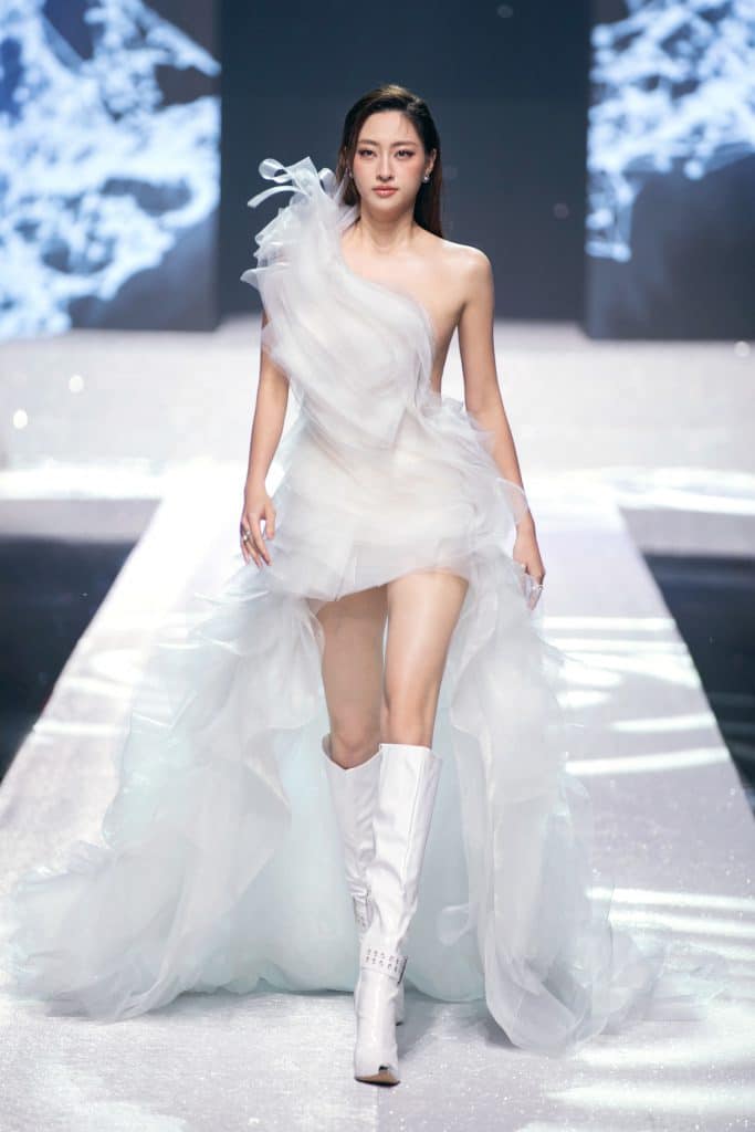 Người mẫu trình diễn váy trắng bồng bềnh trên sàn catwalk sáng đèn
