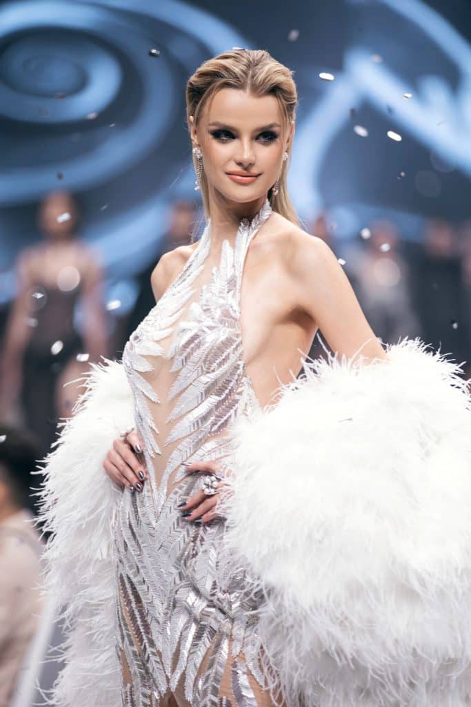 Người mẫu trình diễn trang phục lấp lánh với khăn choàng lông trắng trên sàn catwalk
