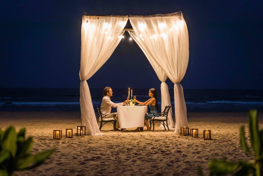 Bữa tối lãng mạn dưới ánh nến trên bãi biển với cặp đôi đang ngồi đối diện nhau