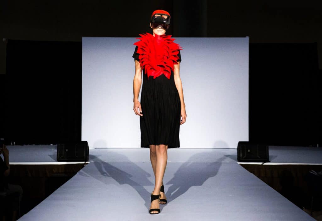 Người mẫu trình diễn trang phục đen và phụ kiện màu đỏ trên sàn catwalk