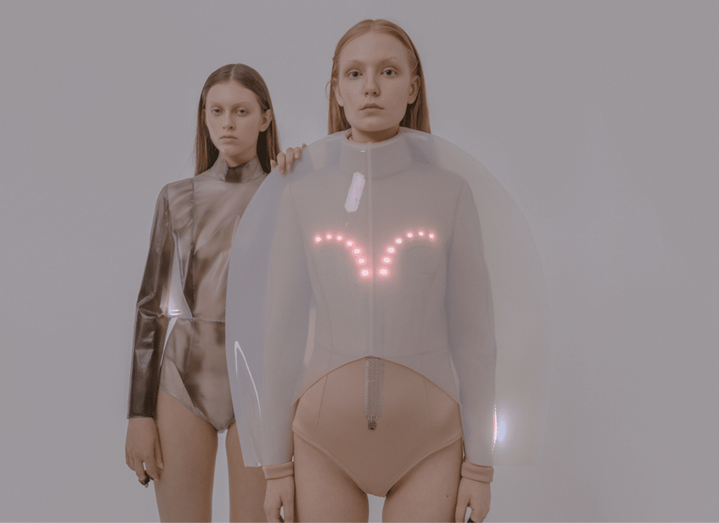 Two women model futuristic clothing with glowing lights and transparent plastic