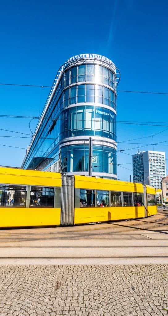 Tàu điện màu vàng chạy ngang qua tòa nhà kính hiện đại ở Dresden