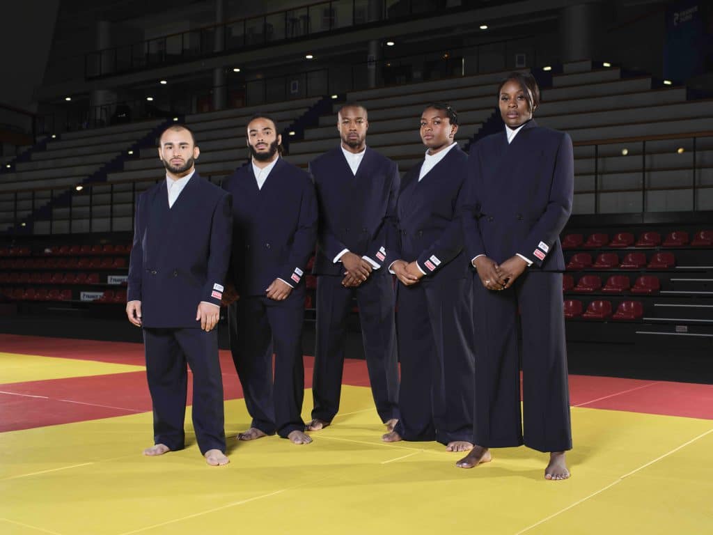 Năm vận động viên judo mặc vest đen đứng trên sàn đấu màu vàng tại Paris