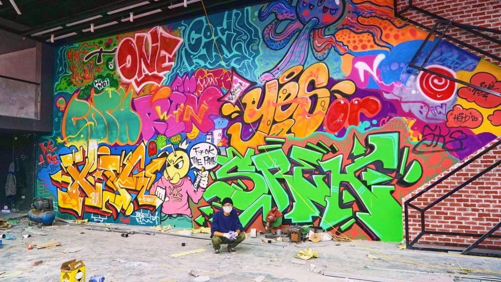 A person sits before a vibrant colorful graffiti mural covering an interior wall