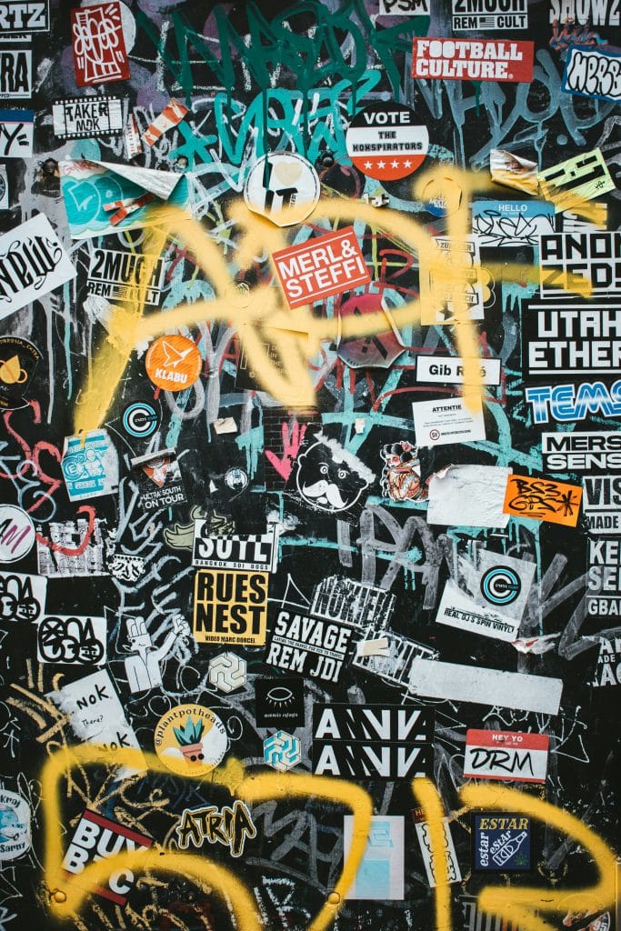 A textured wall is completely covered in colorful stickers and graffiti art