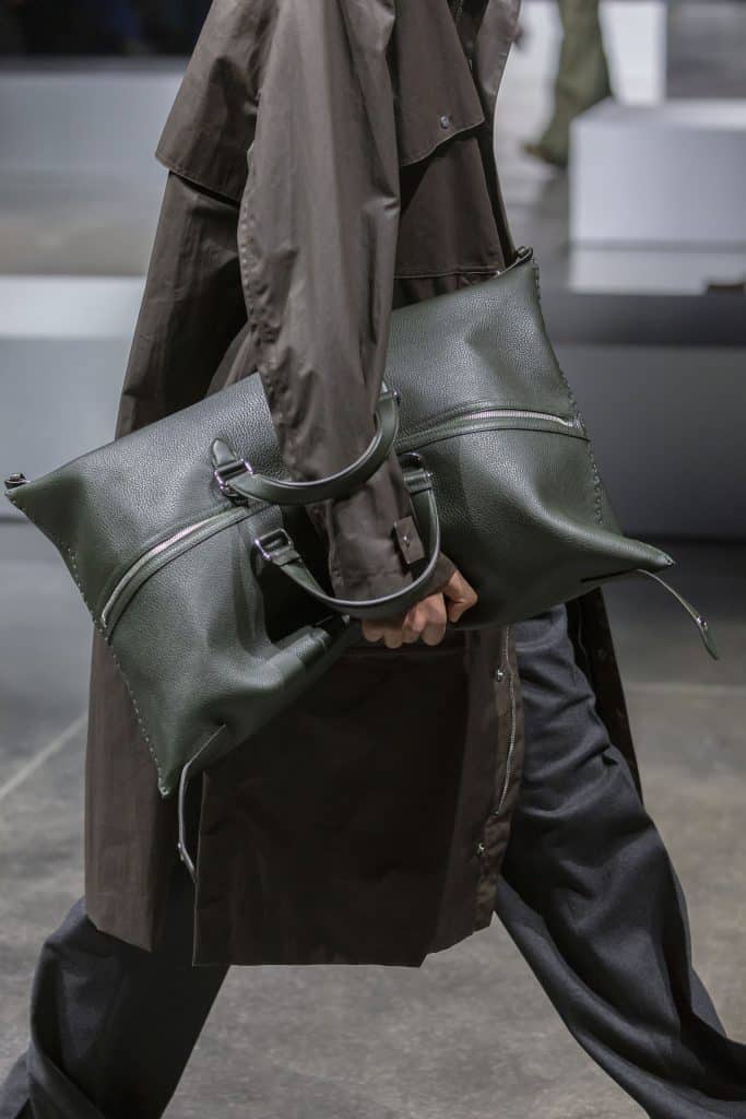 Người mẫu cầm túi xách màu xanh lục đậm đi trên sàn diễn thời trang