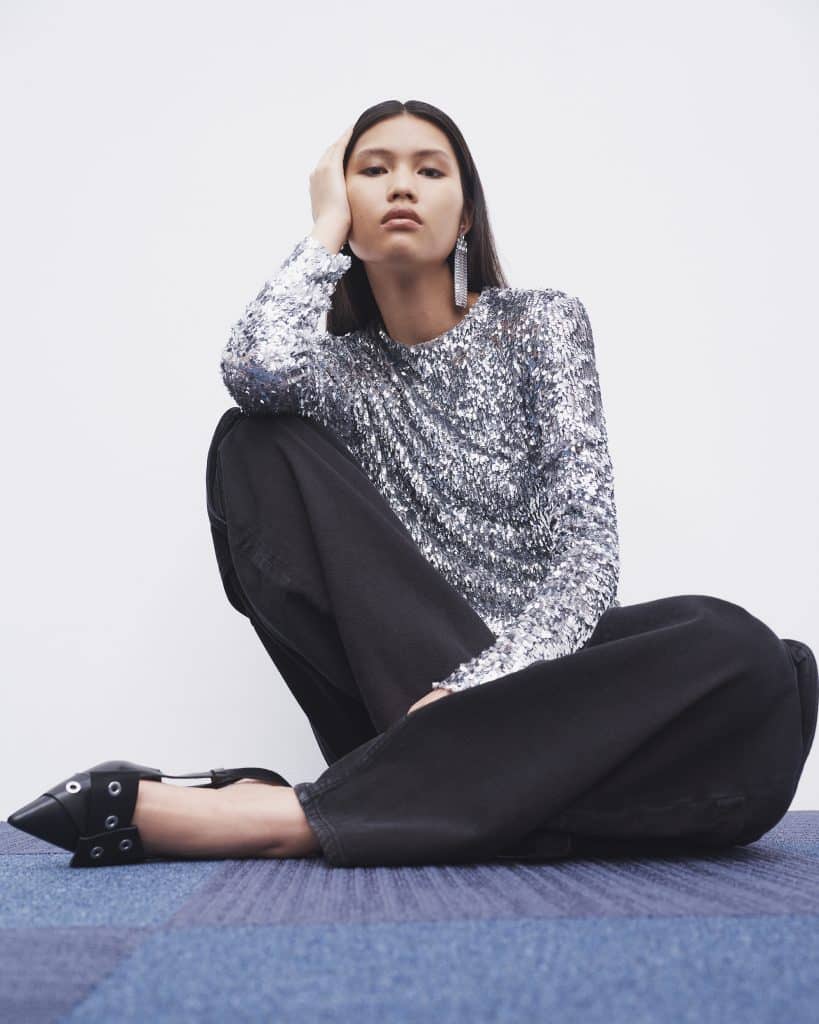 Người mẫu mặc áo sequin lấp lánh và quần đen ngồi trên sàn nhà