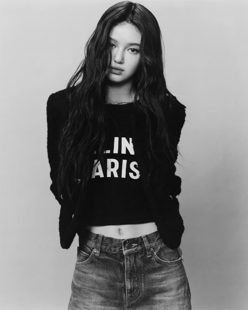 A young woman poses in black clothing with “Paris” printed on her shirt